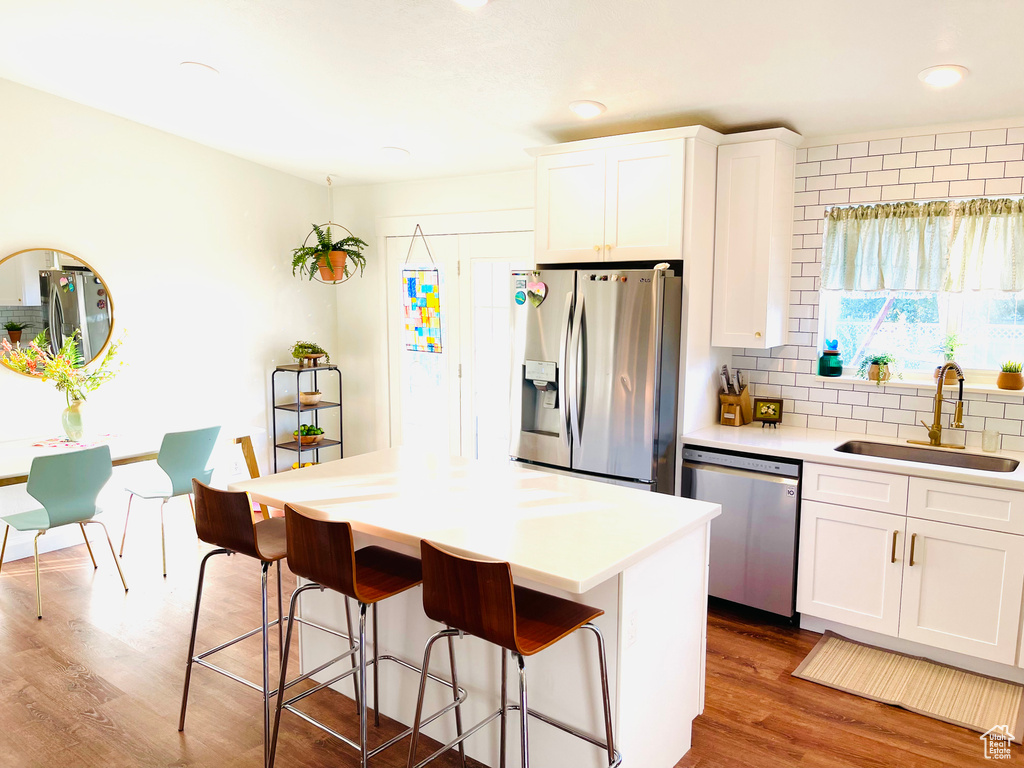 Kitchen featuring appliances with stainless steel finishes, wood finished floors, a kitchen breakfast bar, tasteful backsplash, and white cabinets