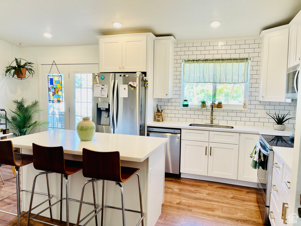 Kitchen with appliances with stainless steel finishes, a center island, white cabinetry, light countertops, and recessed lighting