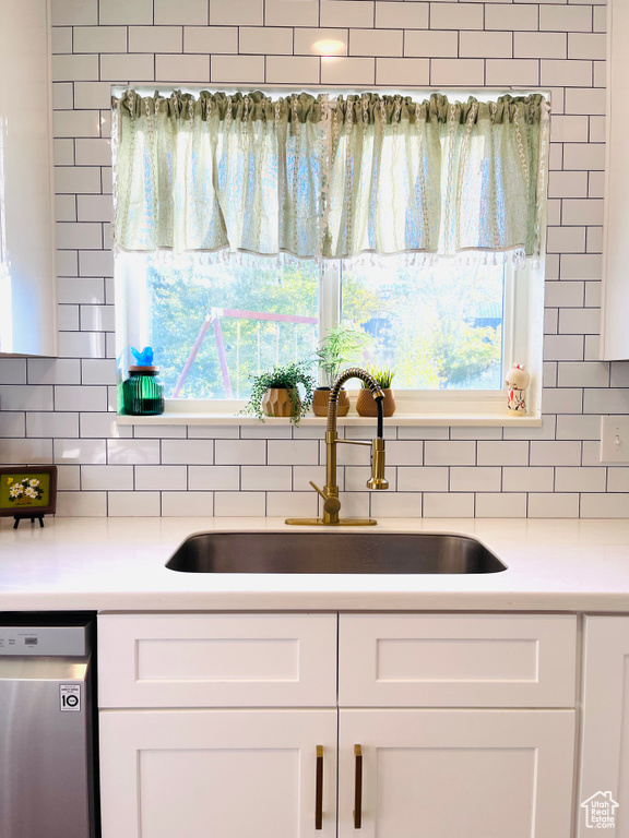 Kitchen featuring stainless steel dishwasher, decorative backsplash, white cabinetry, and light countertops