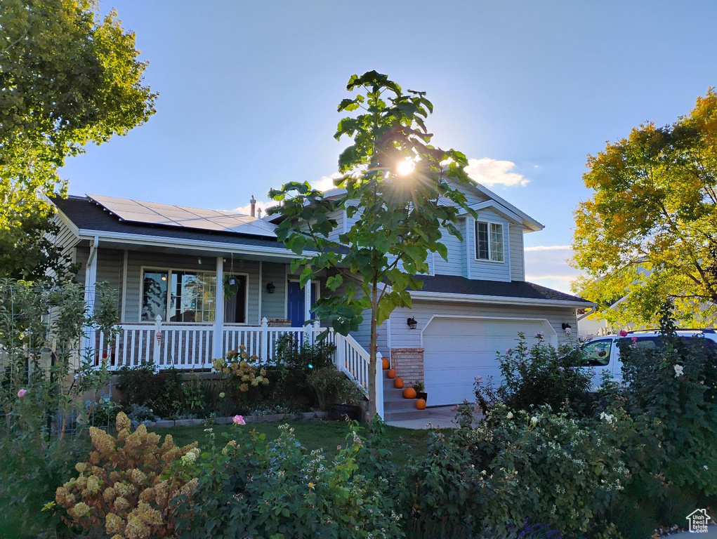 View of front of property with a porch, an attached garage, and solar panels