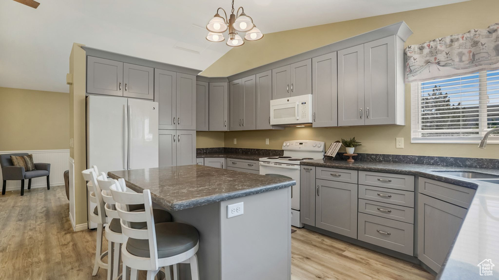 Kitchen featuring white appliances, gray cabinets, a center island, light wood finished floors, and lofted ceiling