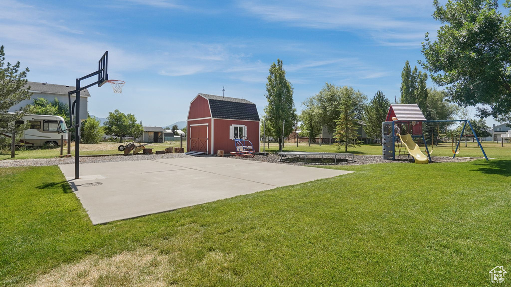 View of sport court featuring a lawn, a playground, basketball court, and a barn