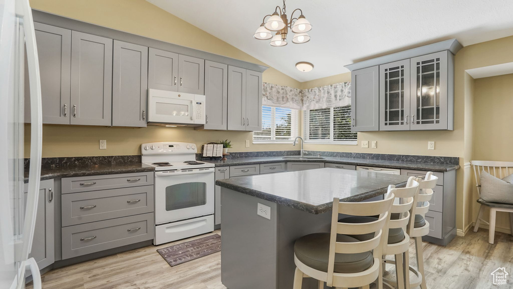 Kitchen featuring white appliances, gray cabinetry, lofted ceiling, a kitchen bar, and light wood-style flooring
