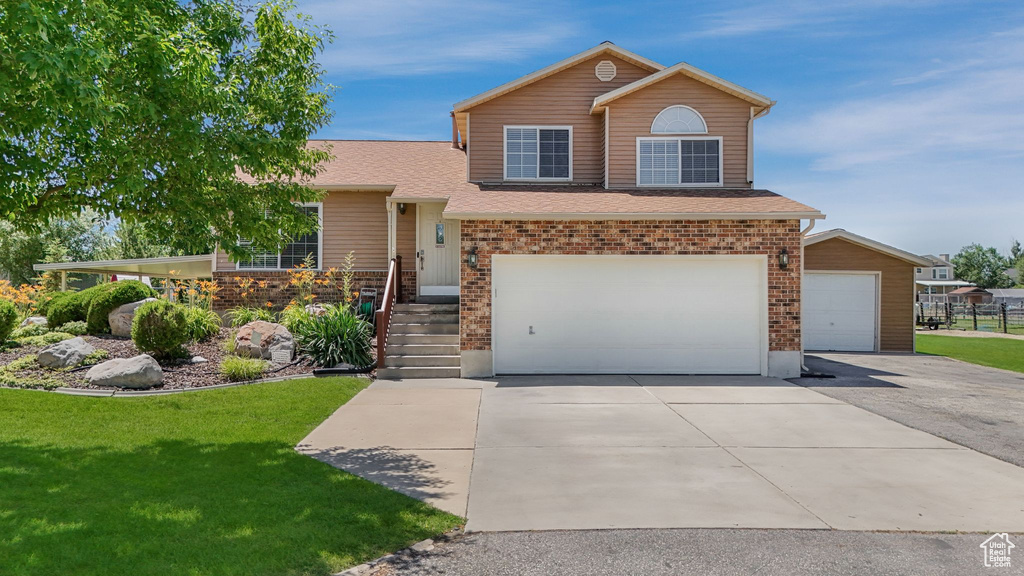 Tri-level home with a front lawn, an attached garage, brick siding, and driveway