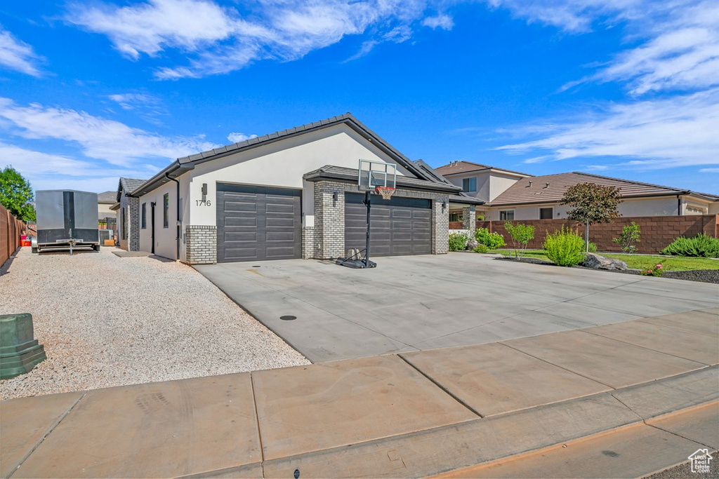 View of front of property featuring an attached garage, driveway, stucco siding, a residential view, and brick siding