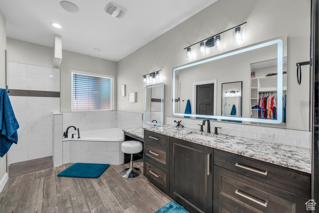 Bathroom featuring a garden tub, vanity, wood finished floors, walk in shower, and a walk in closet