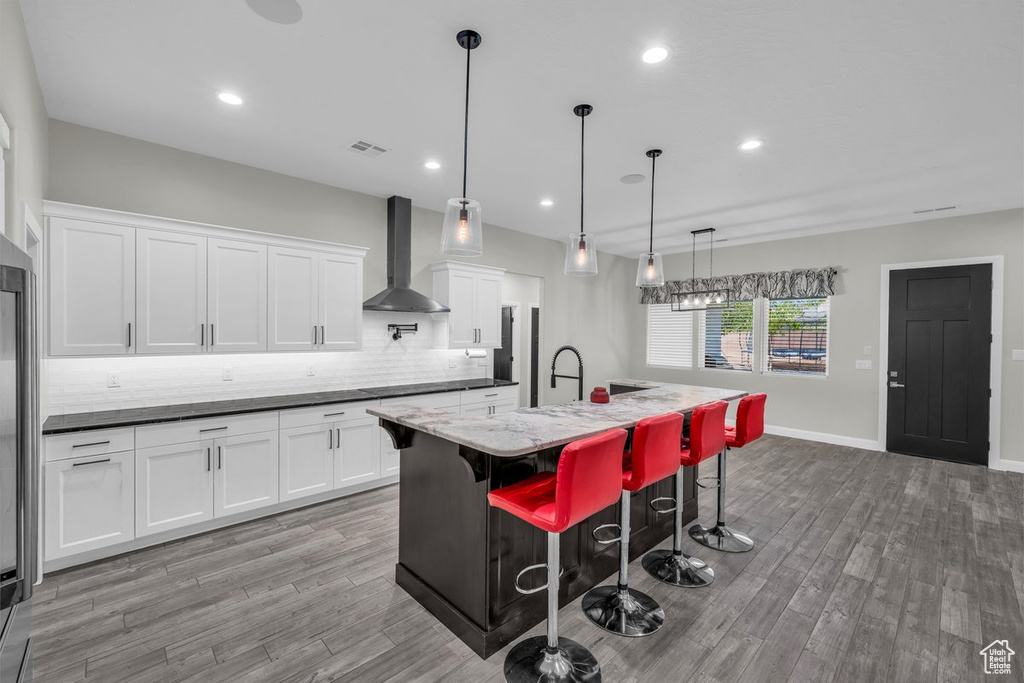 Kitchen with wall chimney range hood, backsplash, light wood-type flooring, white cabinetry, and recessed lighting