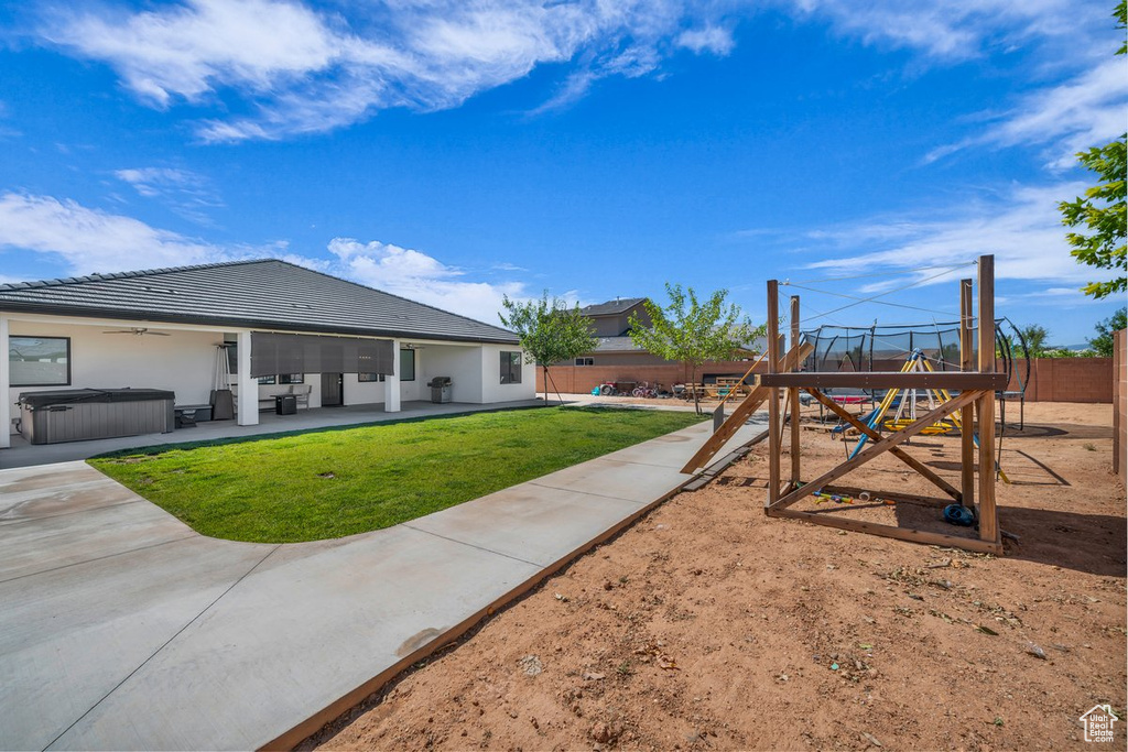 Fenced backyard with a hot tub, a playground, a patio, and ceiling fan