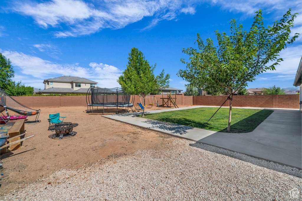 Fenced backyard featuring a trampoline, a playground, and a patio area