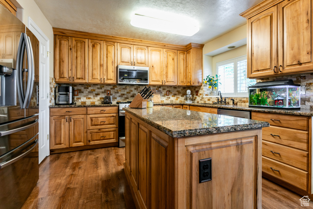 Kitchen with stainless steel appliances, dark wood-type flooring, backsplash, dark stone counters, and a textured ceiling