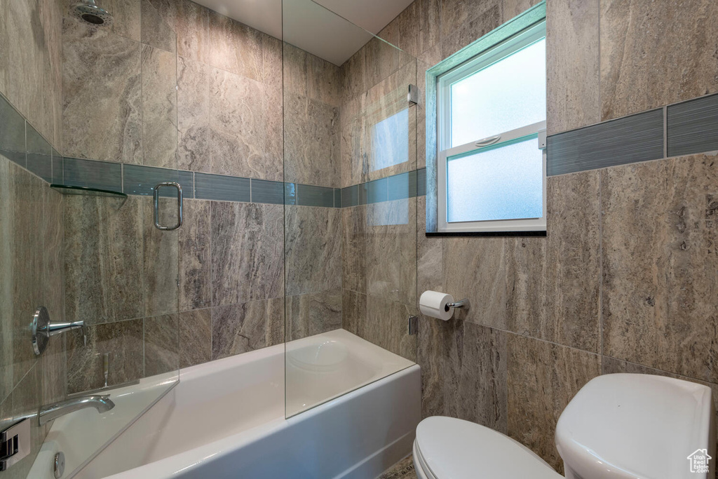 Full bath featuring shower / bath combination with glass door and tile walls