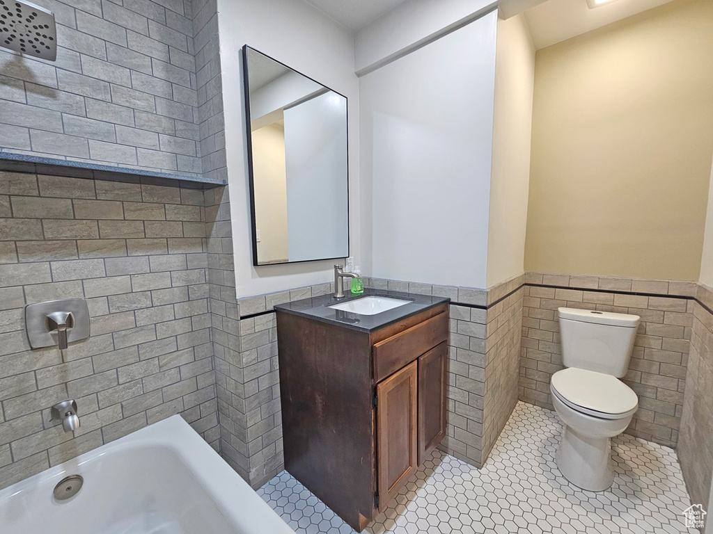 Full bathroom featuring a wainscoted wall, tile walls, a bathtub, vanity, and tile patterned floors