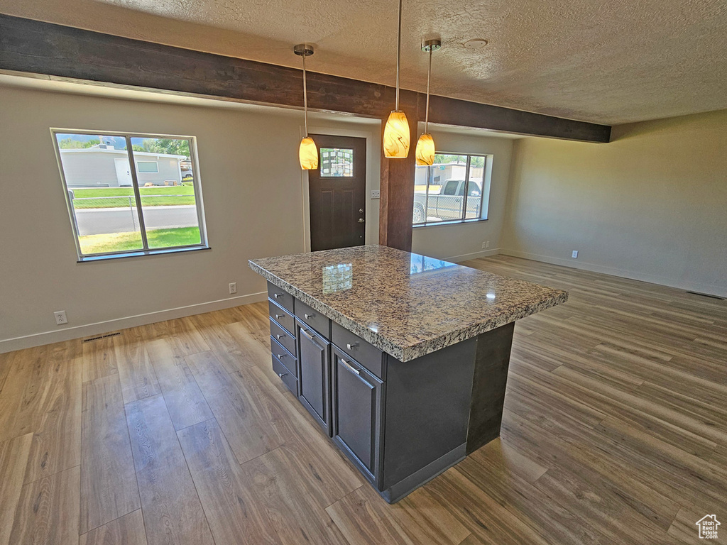 Kitchen with a textured ceiling, wood finished floors, open floor plan, a center island, and decorative light fixtures