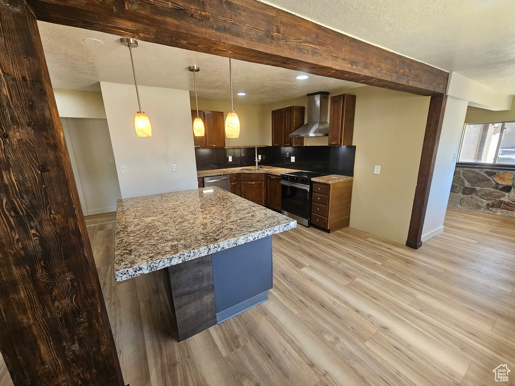 Kitchen with wall chimney range hood, stainless steel appliances, light wood finished floors, a textured ceiling, and tasteful backsplash