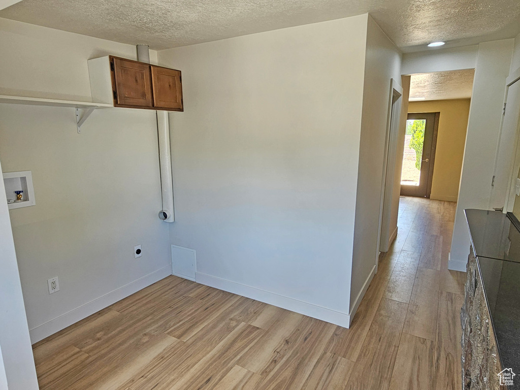 Laundry area with hookup for a washing machine, a textured ceiling, light wood-style flooring, hookup for an electric dryer, and cabinet space