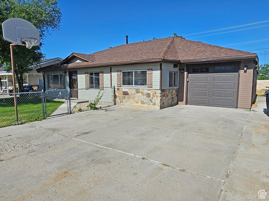 Ranch-style home featuring an attached garage, driveway, stone siding, roof with shingles, and a gate