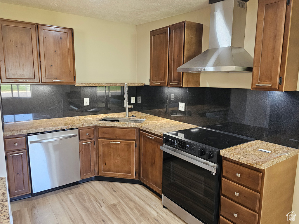 Kitchen featuring stainless steel dishwasher, wall chimney exhaust hood, electric range oven, light wood-style floors, and a textured ceiling