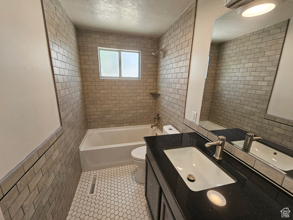 Bathroom with a textured ceiling, vanity, shower / tub combination, tile walls, and tile patterned flooring