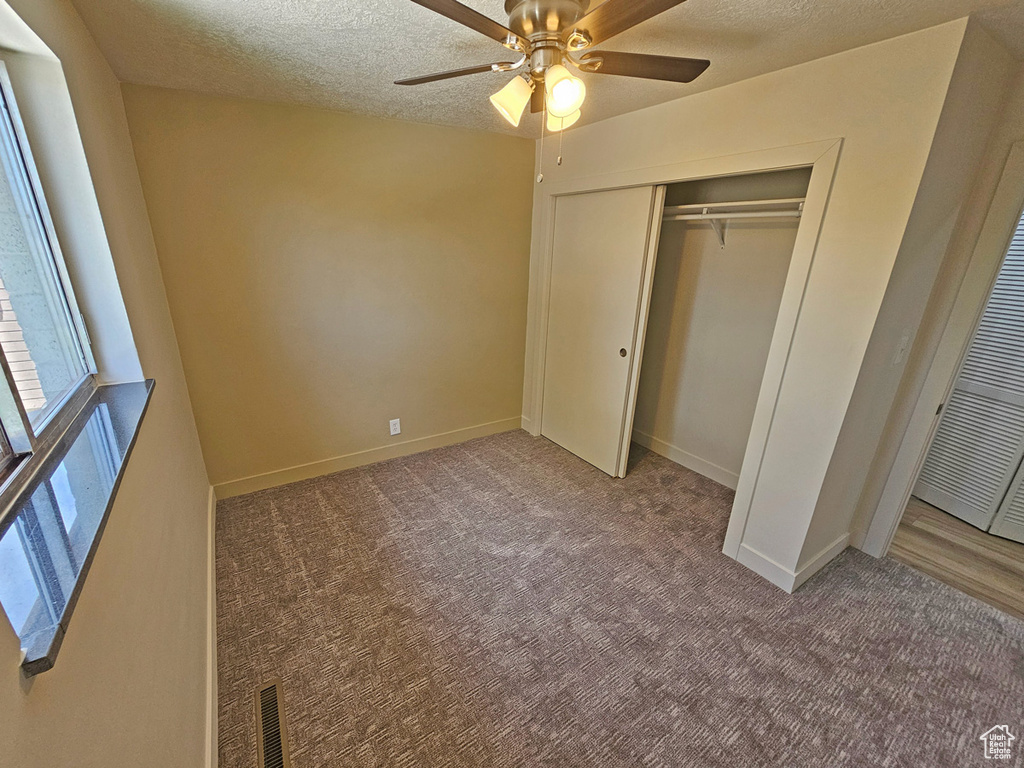 Unfurnished bedroom featuring carpet floors, a textured ceiling, a closet, and ceiling fan