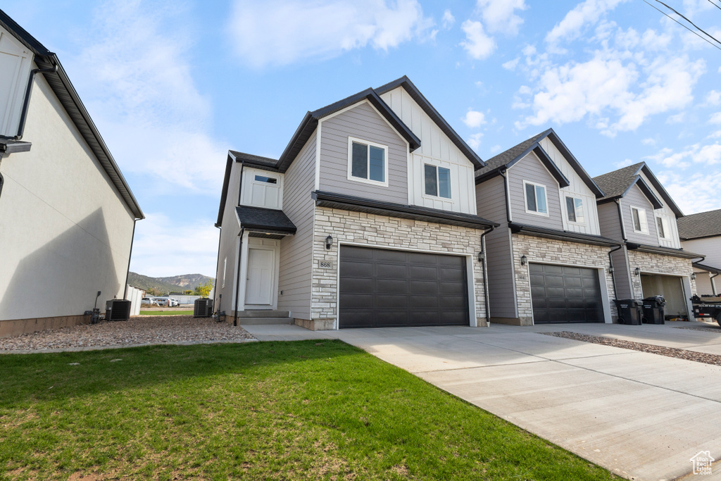 View of front facade with board and batten siding, a garage, a front yard, concrete driveway, and stone siding
