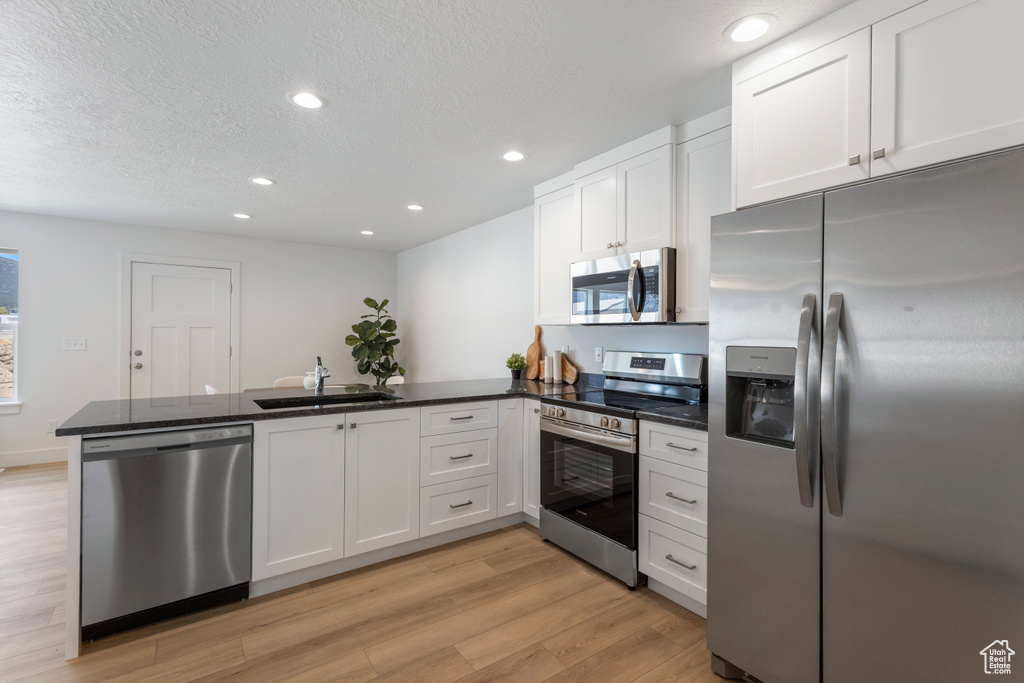 Kitchen with stainless steel appliances, a peninsula, light wood-type flooring, recessed lighting, and white cabinetry