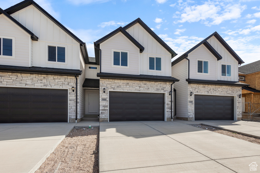 View of front of house with board and batten siding, a garage, concrete driveway, and stone siding