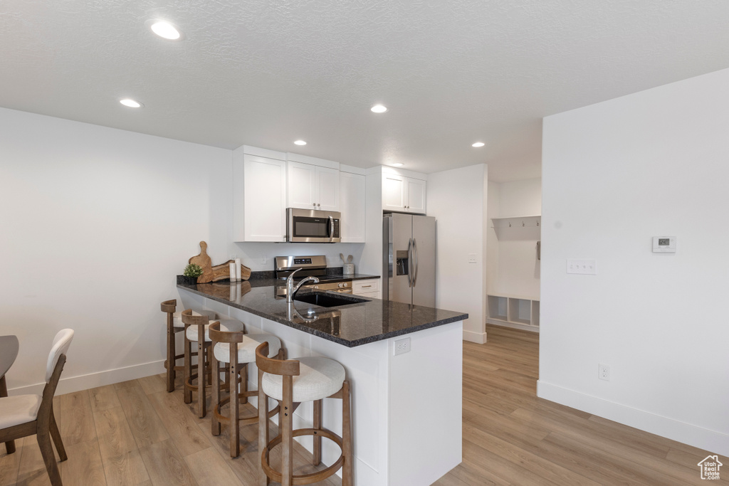 Kitchen with stainless steel appliances, light wood-style flooring, a peninsula, a kitchen bar, and recessed lighting