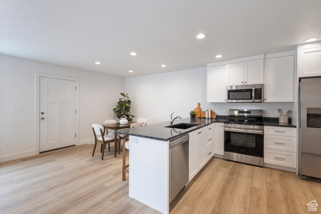 Kitchen with appliances with stainless steel finishes, a peninsula, light wood-style flooring, recessed lighting, and white cabinetry