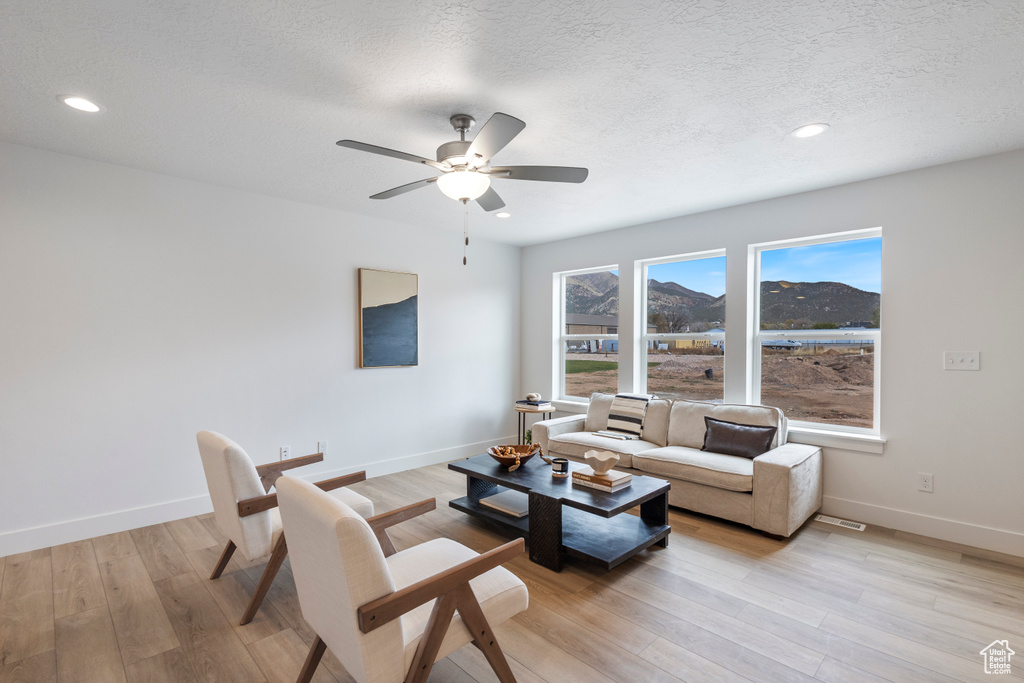 Living area with ceiling fan, light wood-style flooring, recessed lighting, a mountain view, and a textured ceiling