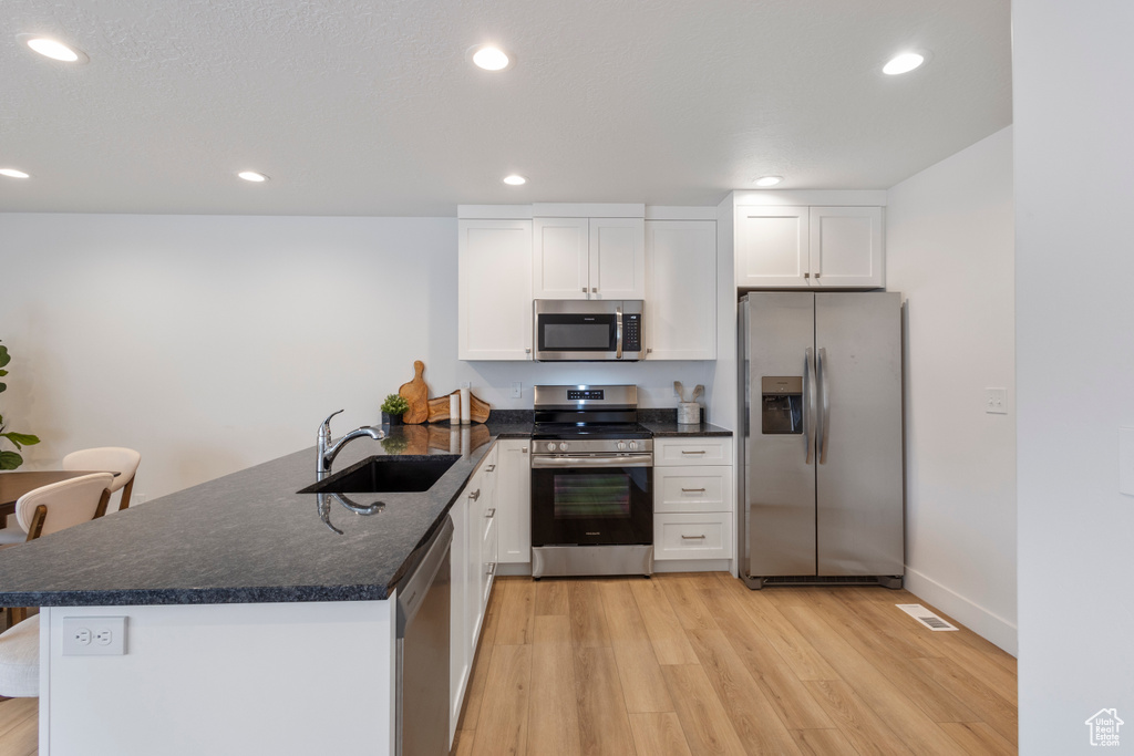 Kitchen with stainless steel appliances, a peninsula, light wood-style flooring, white cabinetry, and recessed lighting