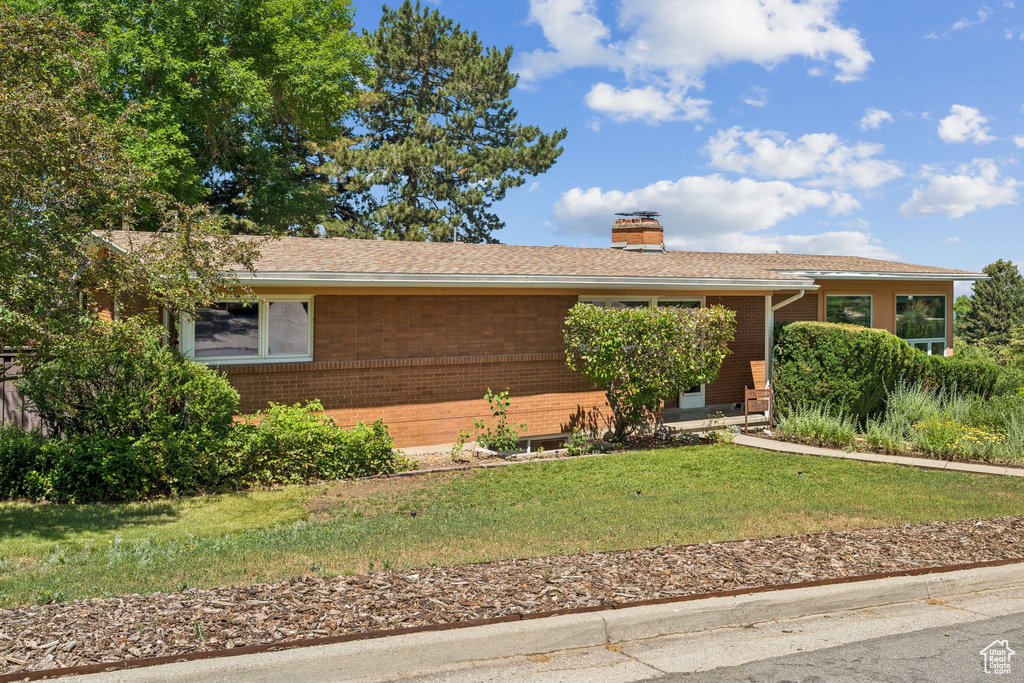 Single story home featuring brick siding, a chimney, and a front yard