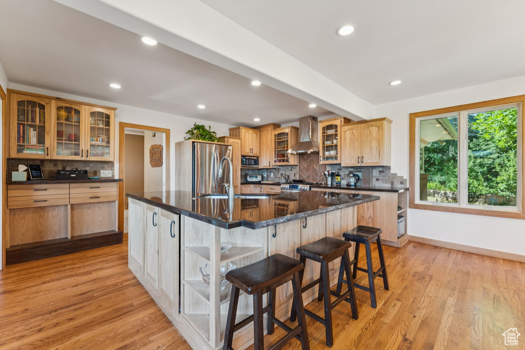 Kitchen with appliances with stainless steel finishes, wall chimney exhaust hood, decorative backsplash, light wood-type flooring, and recessed lighting