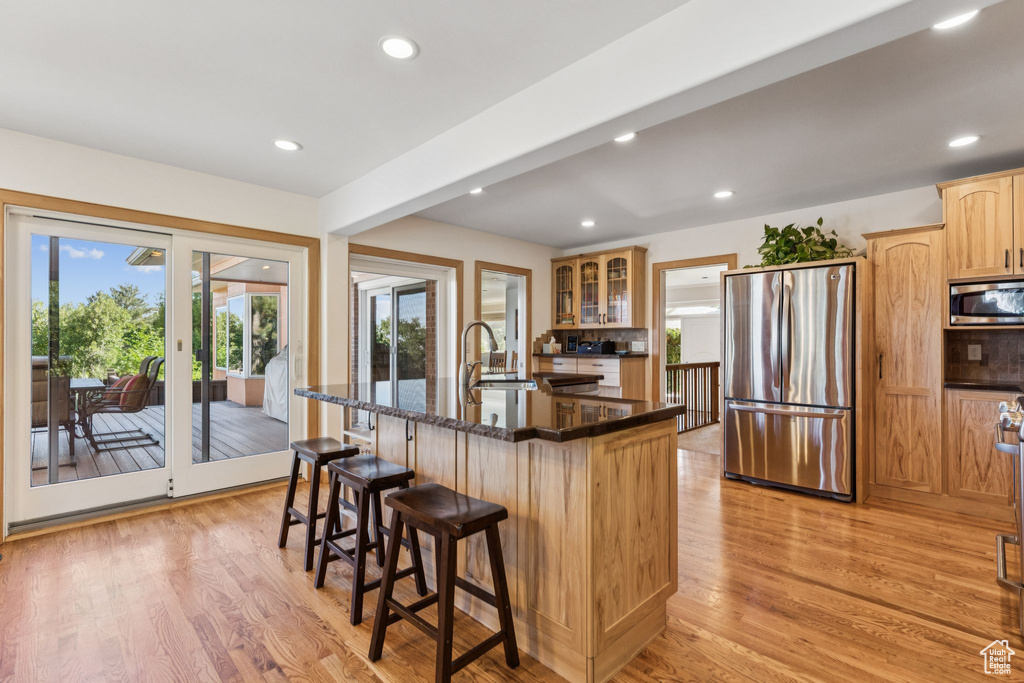 Kitchen with appliances with stainless steel finishes, light wood-style floors, a kitchen breakfast bar, light brown cabinetry, and a center island with sink