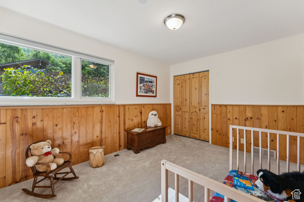 Carpeted bedroom with wooden walls, wainscoting, and a closet