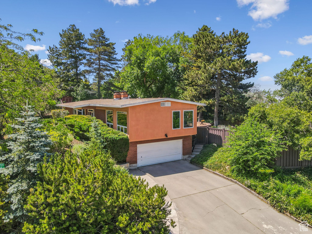 View of front facade with a garage, driveway, a chimney, and view of wooded area