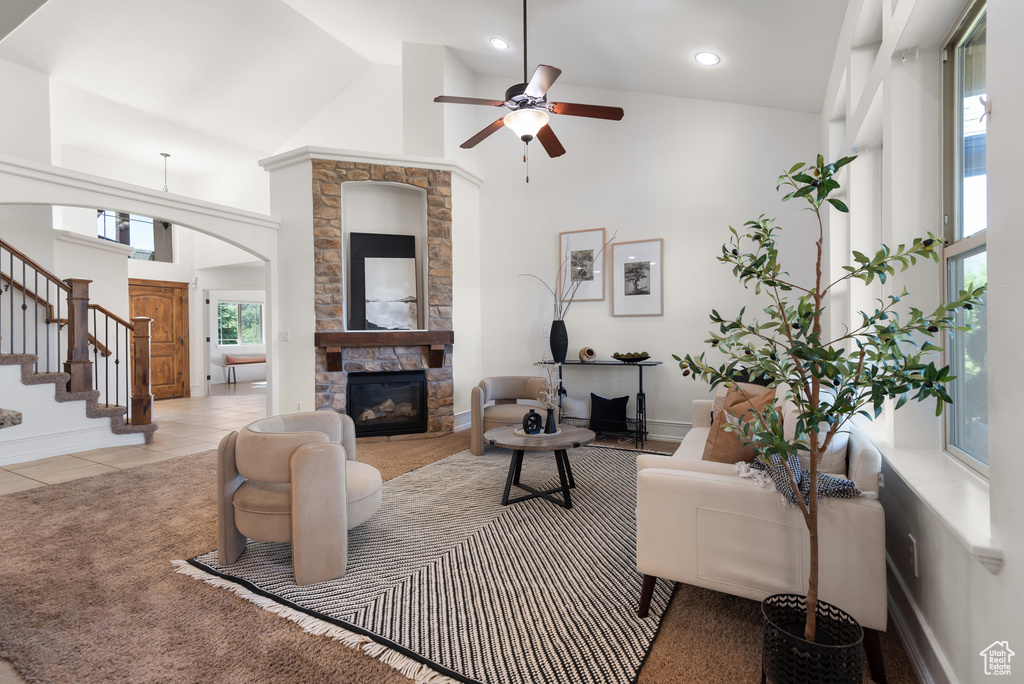 Tiled living area featuring arched walkways, ceiling fan, a fireplace, high vaulted ceiling, and stairs