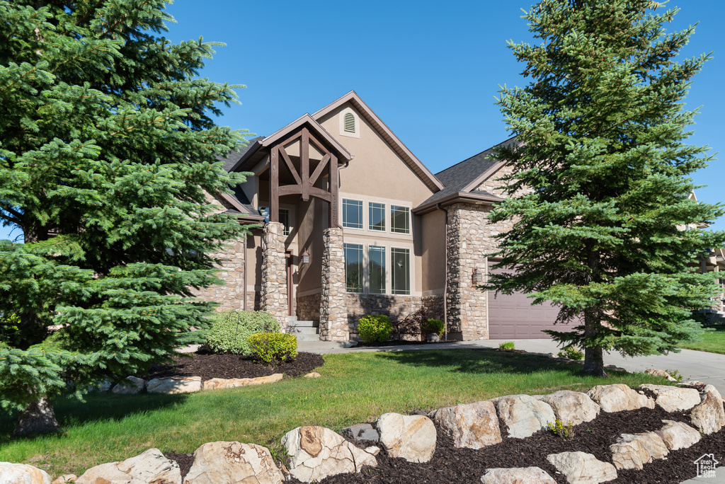 Tudor home featuring stone siding, stucco siding, a front yard, and concrete driveway