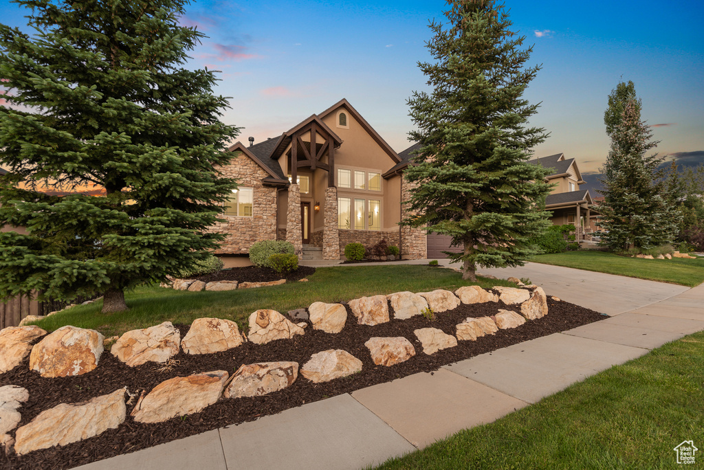English style home with stone siding, stucco siding, a front yard, and driveway