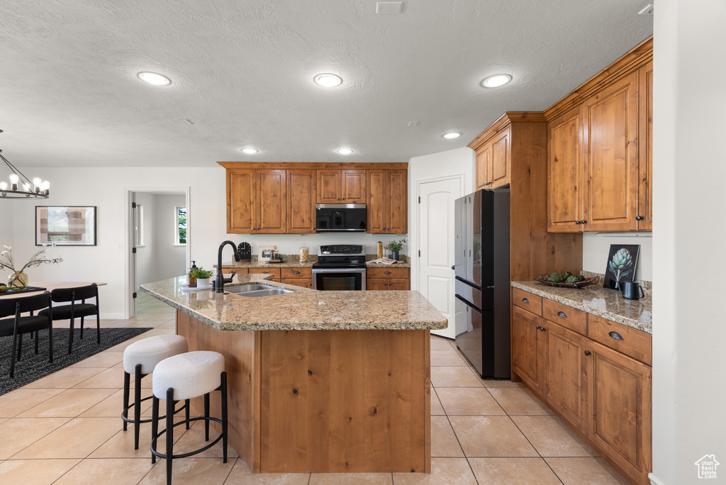Kitchen with appliances with stainless steel finishes, light tile patterned floors, a center island with sink, brown cabinetry, and recessed lighting