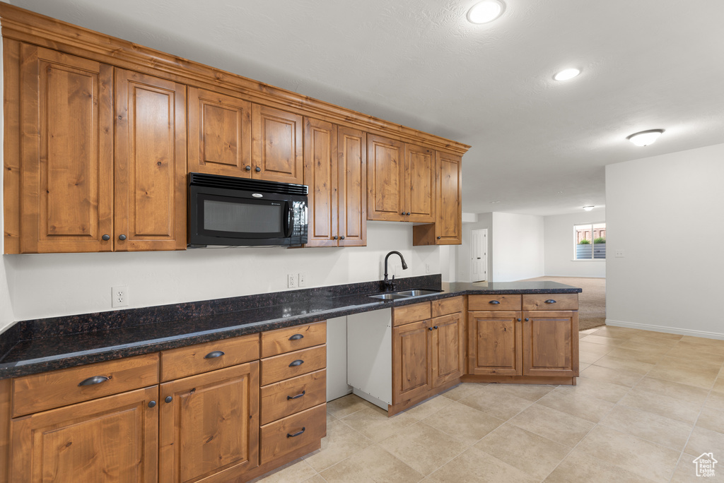 Kitchen featuring black microwave, a peninsula, brown cabinetry, dark stone counters, and recessed lighting