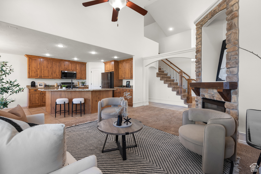 Living room featuring a stone fireplace, a towering ceiling, stairs, recessed lighting, and ceiling fan