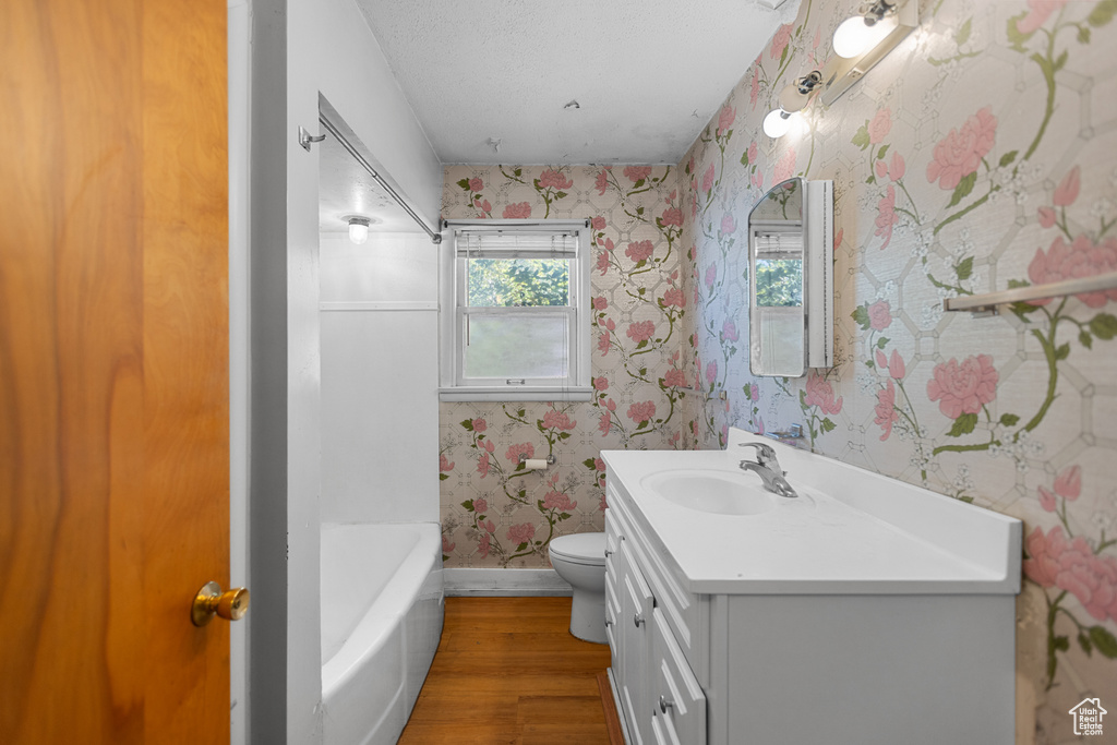 Full bath featuring wallpapered walls, vanity, wood finished floors, a tub, and a shower