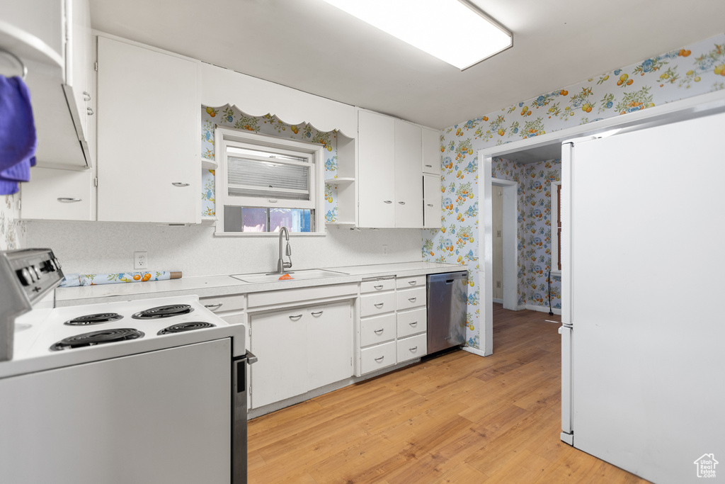 Kitchen with white appliances, wallpapered walls, light countertops, light wood finished floors, and white cabinets
