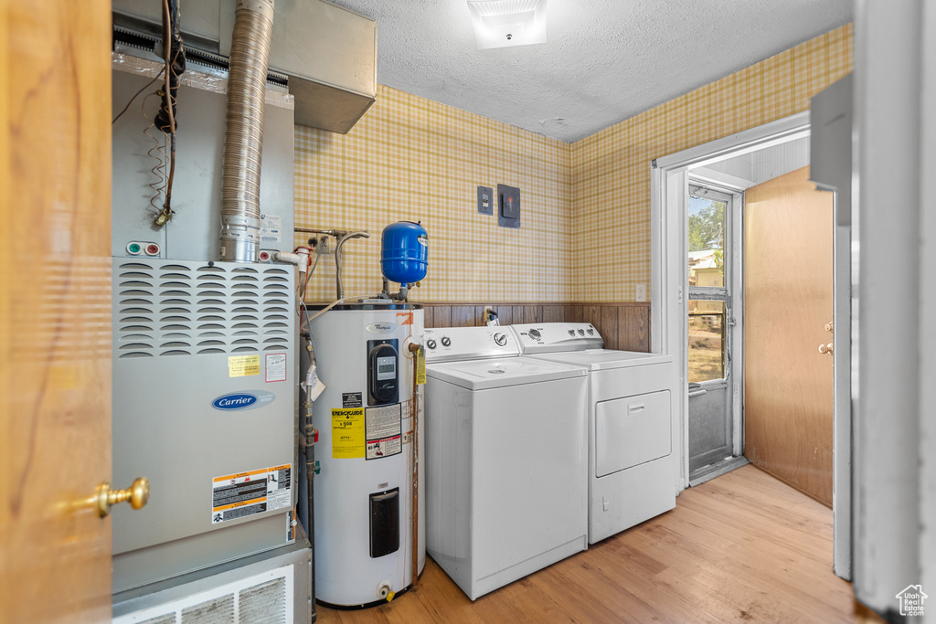Washroom with water heater, washing machine and clothes dryer, wallpapered walls, light wood-style flooring, and a textured ceiling