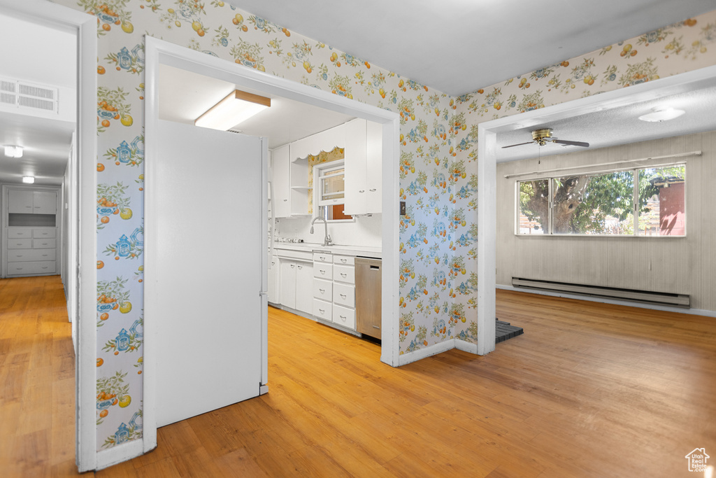 Kitchen with a baseboard heating unit, stainless steel dishwasher, wallpapered walls, light wood finished floors, and white cabinets