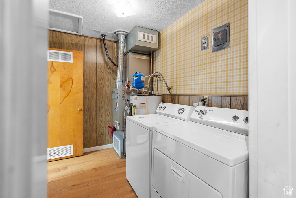 Washroom with independent washer and dryer, wallpapered walls, light wood-style flooring, electric water heater, and a textured ceiling