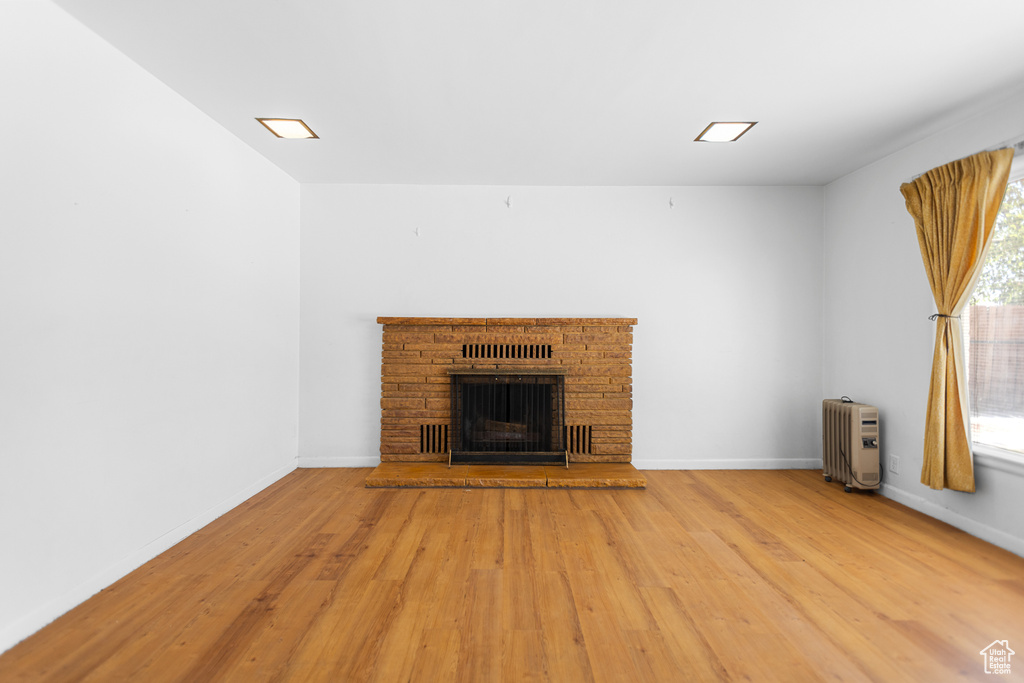 Unfurnished living room featuring radiator heating unit, wood finished floors, and a fireplace with raised hearth
