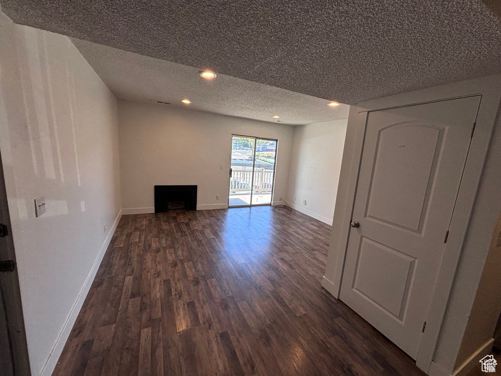 Unfurnished living room featuring dark wood-style floors, a textured ceiling, a fireplace, and recessed lighting
