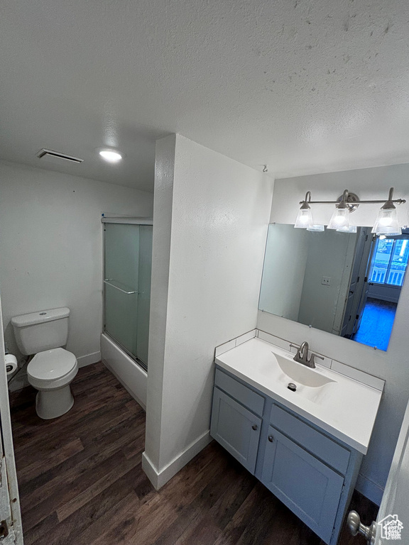 Bathroom with wood finished floors, vanity, bath / shower combo with glass door, and a textured ceiling