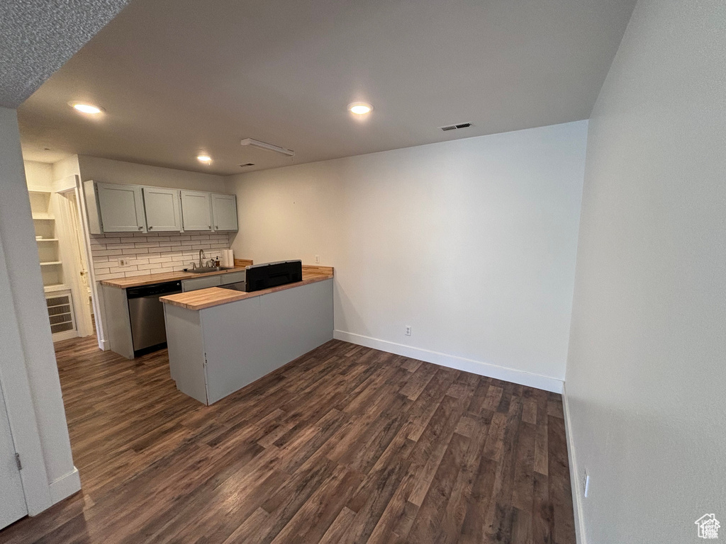 Kitchen featuring dark wood finished floors, a peninsula, backsplash, stainless steel dishwasher, and recessed lighting